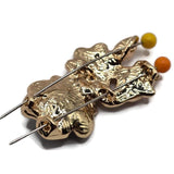 Detailed view of bright gold floral slider beads showcasing contrasting charcoal-black, soft pink, peach, and pearl white enamel. The larger dark flower features softly textured petals and a brilliant clear rhinestone center, while smaller pastel flowers and pearlescent leaves complete the botanical design. Polished gold outlines add warmth and shine to these decorative jewelry-making components.